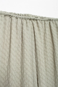 Detail of sage green crinkle fabric with elastic smocking on the waist of a v-neck top