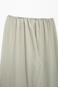 Detailed view of elastic waistband on textured wide leg trousers in pale beige fabric