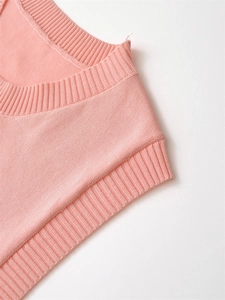 Macro detail of fine knit texture and ribbed V-neckline on light pink sleeveless vest