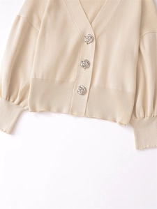 Close-up of beige knit cardigan featuring decorative silver rose-shaped metal buttons