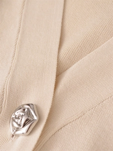 Detail of silver rose metal button on beige knit cardigan with soft fabric texture