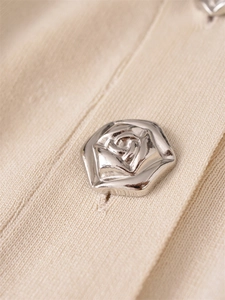 Close-up of a vintage silver rose-engraved metal button on beige knit cardigan fabric