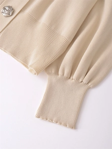 Detail of floral silver metal button and ribbed knit texture on beige cardigan