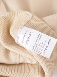 Detail of the 100% polyester fabric material label on a cream knitted cardigan