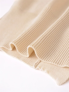 Close-up of beige rib-knit hem showing the detailed vertical knit texture of the sweater