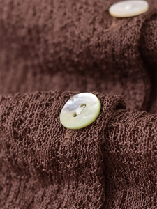 Macro shot of dark brown knit fabric with delicate hollow weave and pearl buttons