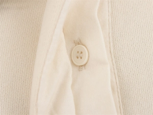 Makroaufnahme eines cremefarbenen Strick-Polo-Sweatshirts mit detailliertem Vierloch-Knopf