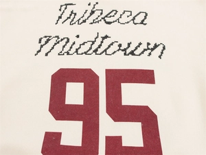 Detail eines cremefarbenen Polo-Sweatshirts mit Tribeca-Aufdruck und weinroter Nummer 95