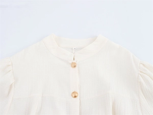 Detail der cremeweißen Textur-Bluse mit Stehkragen und geprägten Goldknöpfen