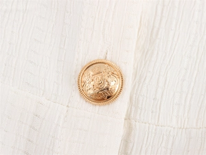 Makro-Detail des weißen Jacquard-Stoffs und des goldenen Knopfes mit Löwenwappen
