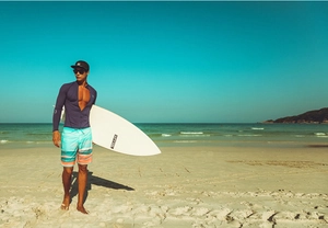 Deep purple long sleeve surf top and striped light blue swim trunks on a beach