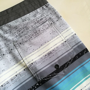 Detail of men beach shorts showing back pocket with button and striped ink splash fabric