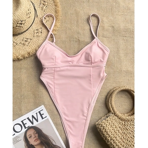 Flat lay of pale pink high-cut swimsuit with thin straps on rustic summer beach accessories