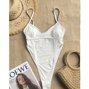 Flat lay of white v-neck bodysuit with thin straps on rustic burlap and summer props
