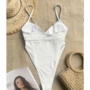 Flat lay of white high-cut one-piece swimsuit with thin straps on beige linen background