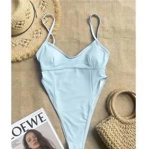 Flat lay of light blue one-piece swimsuit with high-cut design and summer accessories