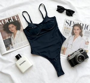 Flat lay of black underwire one-piece swimsuit with spaghetti straps on white fabric