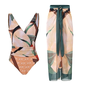 Flat lay of a V-neck tropical leaf one-piece swimsuit with a matching sheer sarong skirt