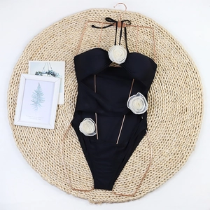 Flat lay of black halter one-piece swimsuit featuring 3D white mesh flowers and a gold hanger
