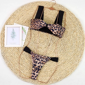 Flat lay detail of leopard print bikini set with black straps on a woven mat
