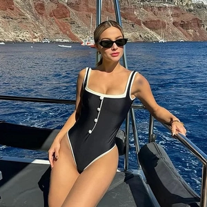 Detail of black one-piece swimsuit with white contrast piping and decorative buttons
