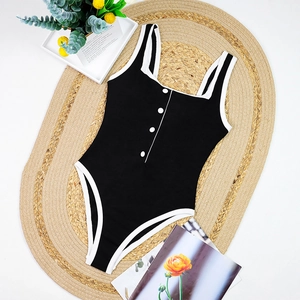 Detail of black ribbed swimsuit with white trim and four decorative buttons on front