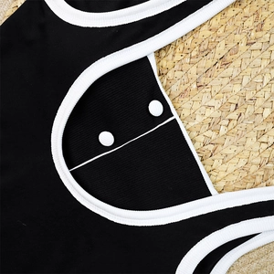 Detail of black ribbed swimsuit with white trim and decorative buttons on straw mat