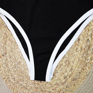 Close-up of black ribbed swimsuit fabric with white contrast piping on woven straw mat