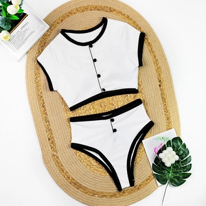 Detailed flat lay of a white two-piece bikini with black trim and decorative buttons