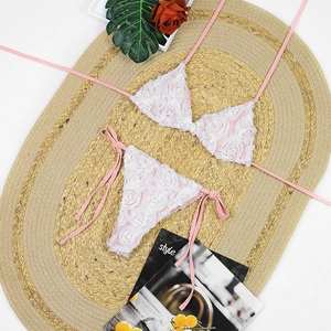 Detailed flat lay of pink and white bikini with 3D floral appliques on a woven mat