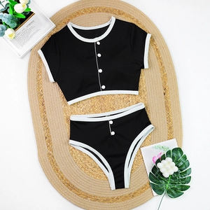 Flat lay of black bikini with white trim and buttons on a straw beach mat