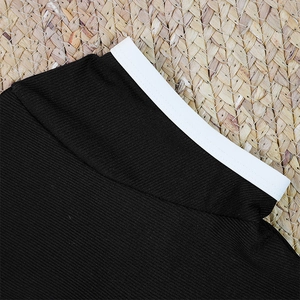 Close-up of black ribbed bikini fabric with white contrast piping on woven mat