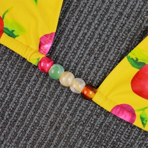 Detail showing the fruit print bikini top with colorful bead connectors and high quality stitching