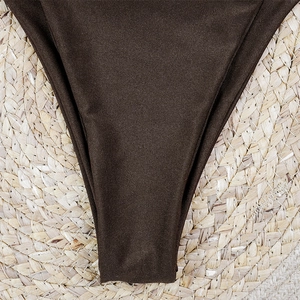 Detail of high-cut dark brown bikini bottom on a natural straw mat background