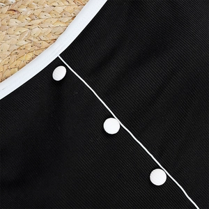 Macro shot of black ribbed bikini fabric with white trim and decorative buttons
