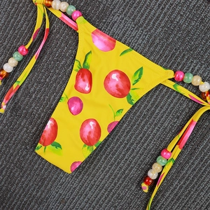 Close-up of yellow bikini bottom with cherry print and colorful beads on side ties