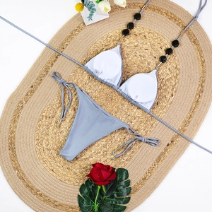 Detail of grey bikini top with black octagonal beads and S size tag on straw mat