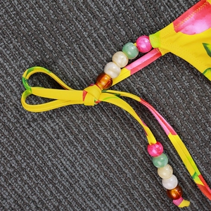 Close-up of yellow floral bikini top with colorful decorative beads and tie details