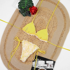 Detail view of yellow bikini with white lace ruffles and 3D floral embellishments on woven mat