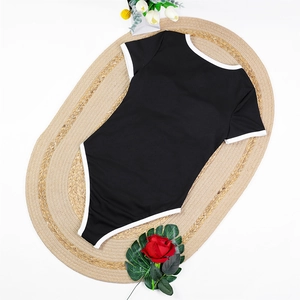 Flat lay of black short sleeve one-piece swimsuit with white trim on woven mat