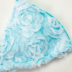 Detailed close-up of 3D white lace rose floral embroidery on aqua blue swimwear fabric