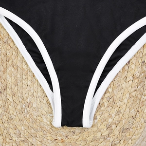 Detail view of black ribbed bikini bottom with white trim on a woven beach mat