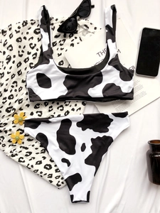 Detailed flat lay of cow print bikini set with stylish fashion accessories on white fabric