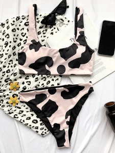 Flat lay of pink cow print bikini set with summer vacation accessories on white fabric