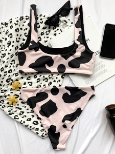 Flat lay of pink cow print bikini with sunglasses and fashion accessories on white fabric
