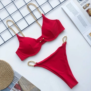 Detailed flat lay of red bikini with gold chain straps on white surface and magazine