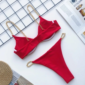 Flat lay of red bikini with gold chain straps on decorative lifestyle background