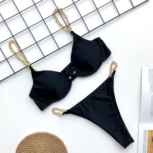 Detail view of black bikini with gold chain straps on textured straw mat background