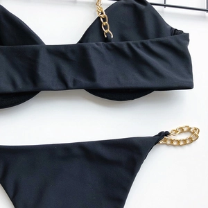 Detail of black bikini set featuring golden chain straps on a flat white background
