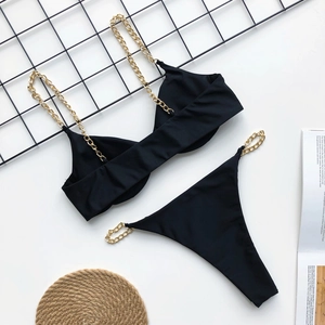 Flat lay of black two-piece bikini featuring gold chain straps and stylish magazine props